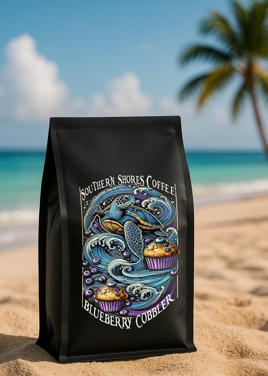 A photo of a blueberry coffee bag sitting in the sand on the beach, the ocean and a palm tree is in the background.