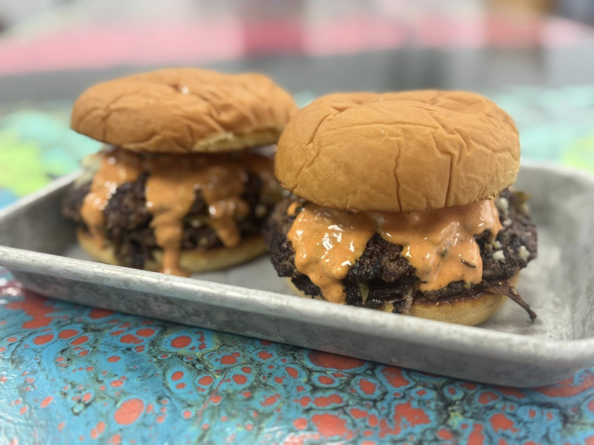 Two cheeseburgers on a metal tray with a colorful background