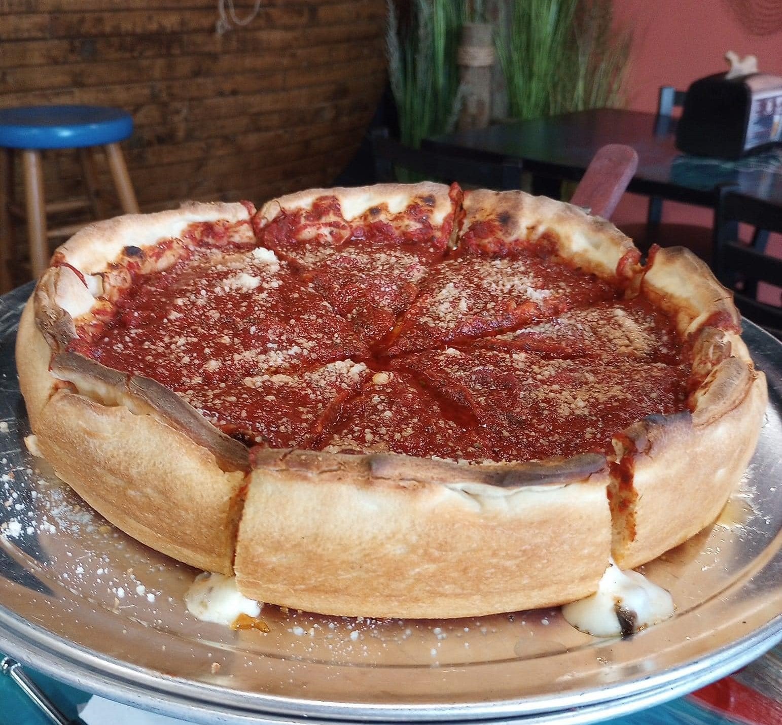 Deep-dish pizza on a metal tray with a casual dining setting in the background