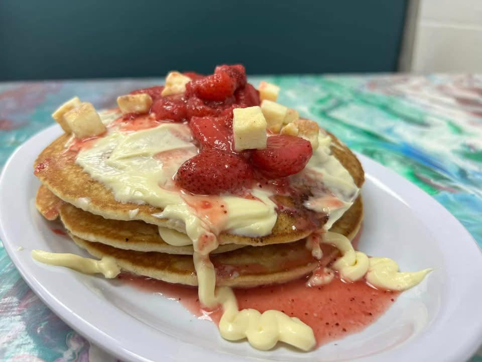 Pancakes covered with strawberries and cheesecake bites on a colorful table 