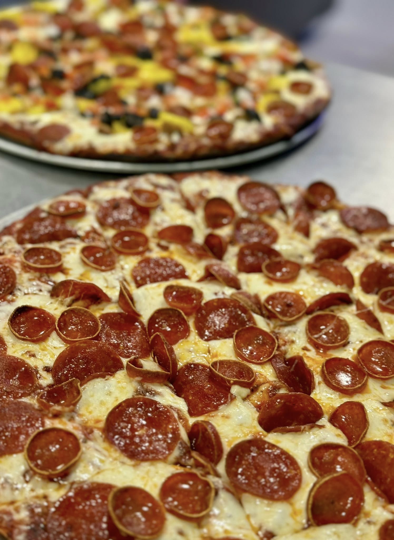 Two pizzas with pepperoni toppings on a table.